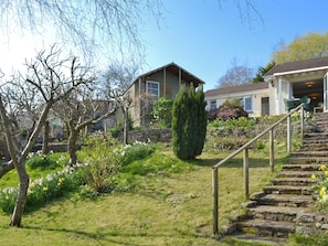 A residential area with stone steps leading to a house, surrounded by greenery and flowering plants.