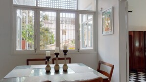 A dining area with a glass table, four chairs, and a window with a view of greenery and buildings. - -APARTMENT CIUDAD VIEJA-PLAZA BOLIVAR THIRD FLOOR- (Cartagena de Indias)