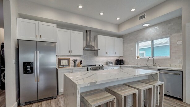 A modern kitchen with white cabinets, a large marble island with bar stools, stainless steel appliances, and a window with a star decoration. - Modern Beauty in Old Town w/Spa Feel.HEATED Private pool-Special Winter discount (Port Aransas)