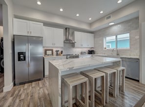 Una cocina moderna con armarios blancos, una isla grande de mármol con taburetes de bar, electrodomésticos de acero inoxidable y un ventanal con un adorno de estrella.