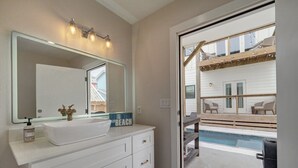 A bathroom with a white vanity, a large mirror, and a view of a pool area with outdoor furniture. - Modern Beauty in Old Town w/Spa Feel.HEATED Private pool-Special Winter discount (Port Aransas)