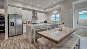 A modern kitchen with white cabinets, a stainless steel refrigerator, a marble countertop, and a wooden dining table with benches. - Modern Beauty in Old Town w/Spa Feel.HEATED Private pool-Special Winter discount (Port Aransas)