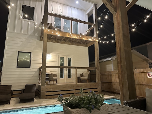 Une maison à deux étages dotée d’un balcon, d’un espace salon extérieur et d’une piscine.