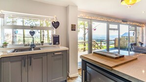 Een moderne keuken met grijze kastjes, een roestvrijstalen koelkast, een raam met uitzicht op de omgeving en een hartvormige decoratie.