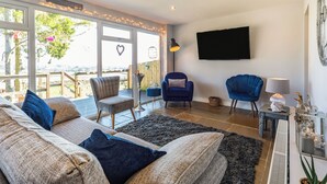Een woonkamer met een bank, stoelen, een televisie en een uitzicht door grote ramen.
