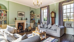 A cozy living room with a fireplace, a sofa, a bookshelf, and a window with curtains.