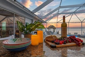 A terrace with a sunset view, a bottle of Stella Rosa wine, fruit, and a candle. - River View, Heated pool - Serenity & Sunrises - Roelens Vacations (Cape Coral)