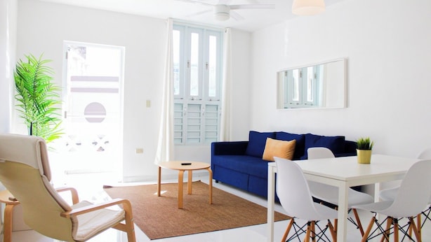 A bright living room with a blue sofa, white chairs, a small round table, and a potted plant. - Arecibo Hotel 2103 (Arecibo)