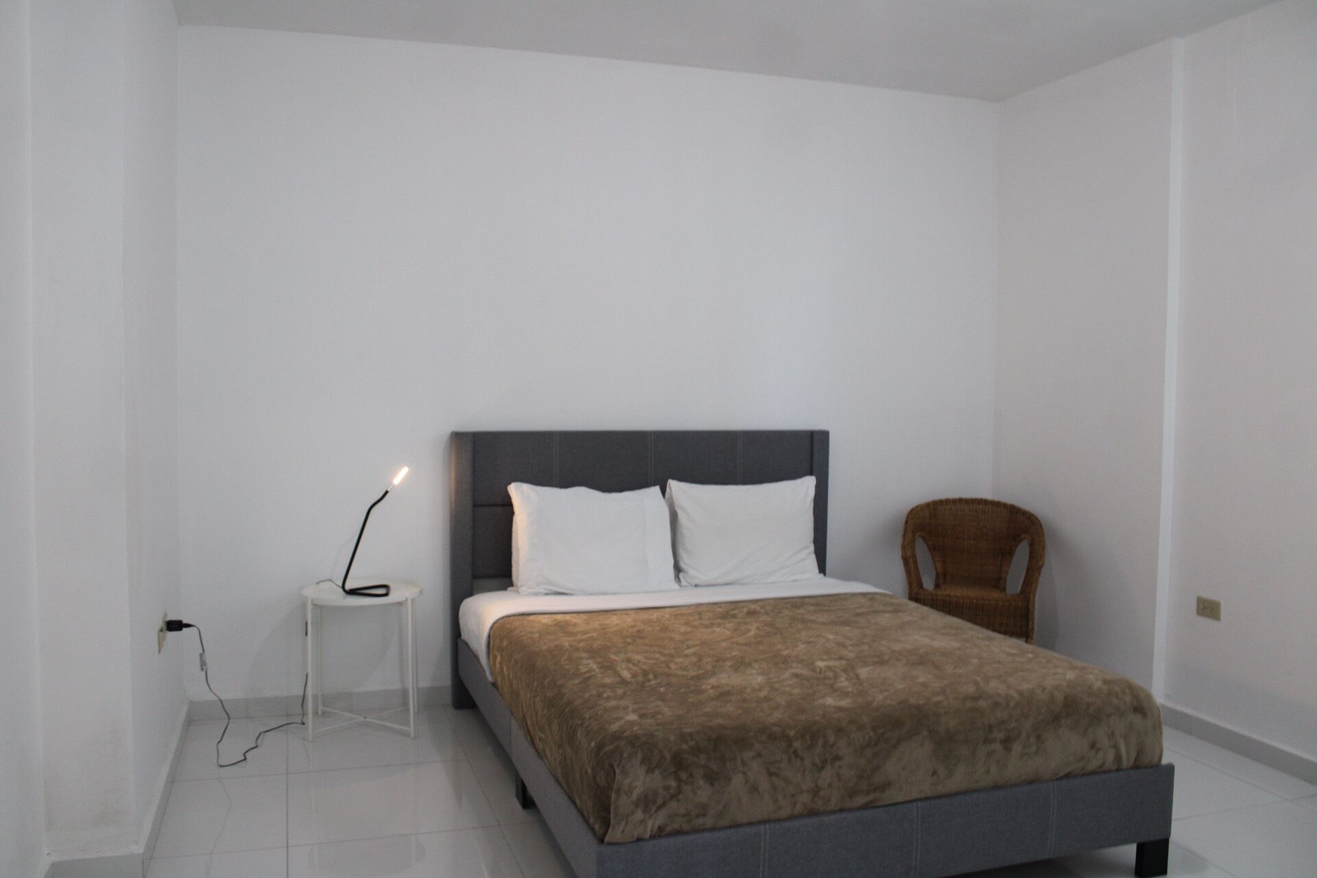 Een slaapkamer met een bed, nachtkastje, lamp en stoel.
