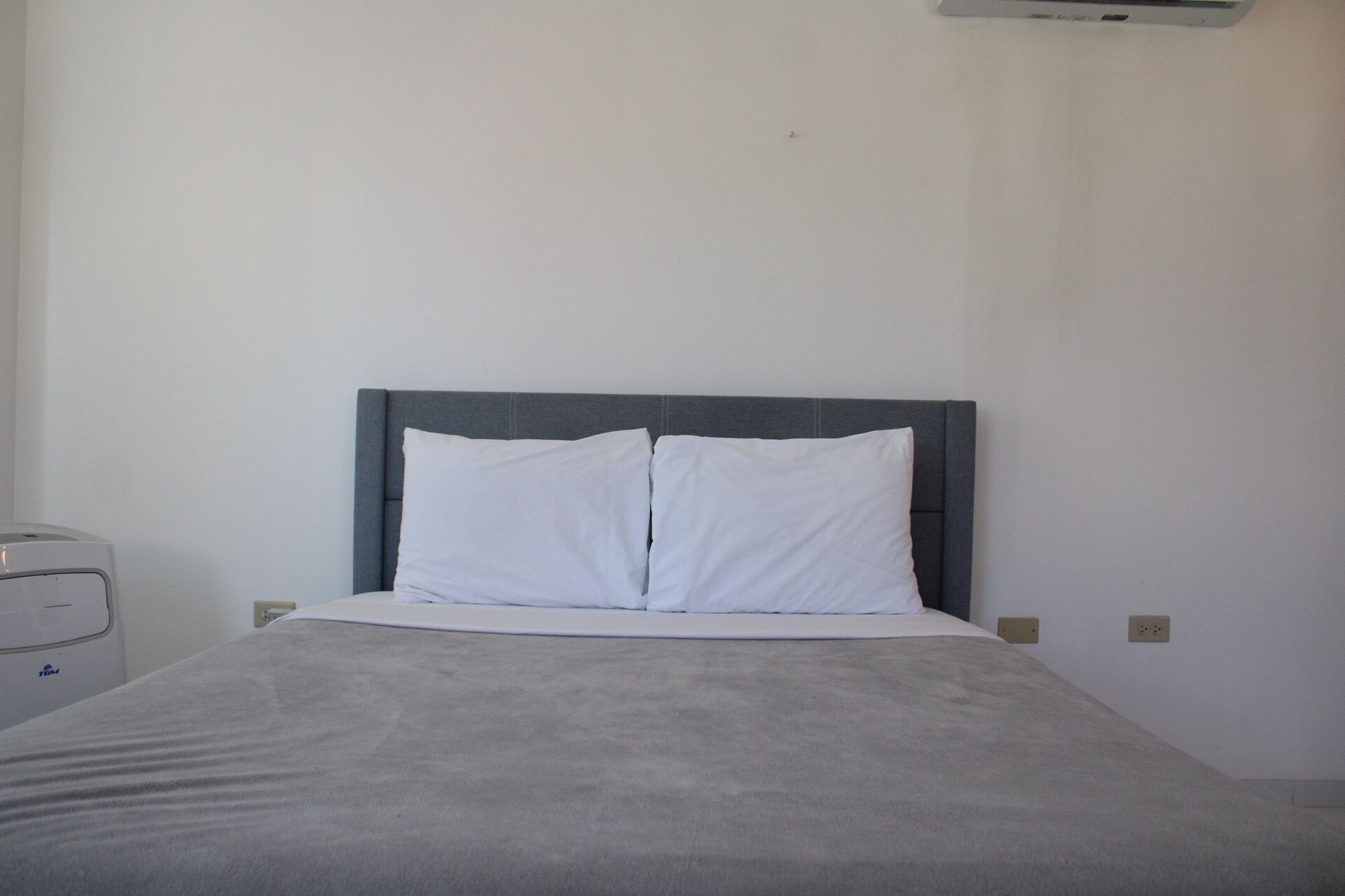 A simple, clean room with a bed, a nightstand, and a wall-mounted air conditioner.