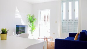 A bright living room with a white table, blue sofa, and a TV on a stand. - Arecibo Hotel 2103 (Arecibo)