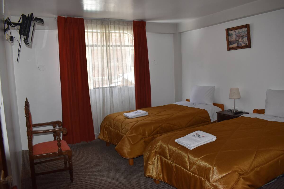 Ett hotellrum med två sängar, en stol, ett skrivbord och ett fönster med gardiner.