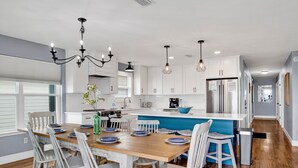 A modern kitchen with white cabinets, a wooden dining table, and a blue accent wall. - Gulf Front Retreat | Beachfront Living | West Beach Favorite (Gulf Shores)