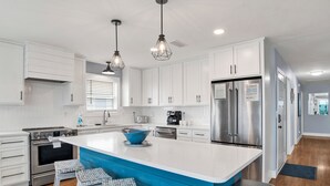 A modern kitchen with white cabinets, a blue island, stainless steel appliances, and bar stools. - Gulf Front Retreat | Beachfront Living | West Beach Favorite (Gulf Shores)
