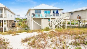 A beachfront house with a balcony, a staircase leading to the upper floor, and a sandy beach in the foreground. - Gulf Front Retreat | Beachfront Living | West Beach Favorite (Gulf Shores)