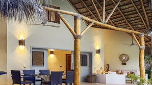 An outdoor seating area with a table and chairs, a thatched roof, and wall-mounted lights.