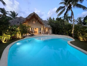 A pool with a curved edge, a thatched-roof building, and palm trees.