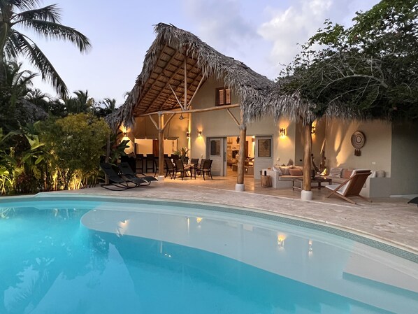 A resort with a pool, lounge chairs, and a thatched-roof building.