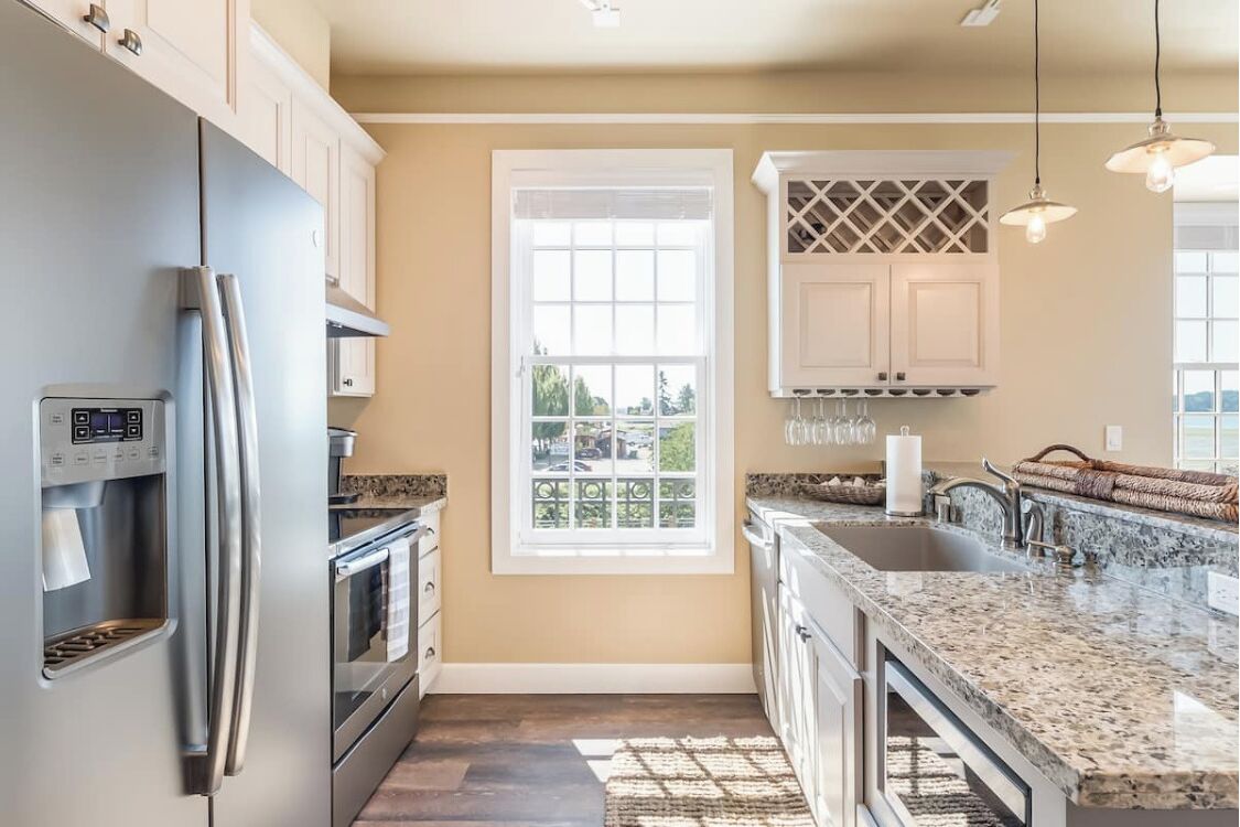 A modern kitchen with a stainless steel refrigerator, built-in oven, granite countertops, and a window with a view of the outdoors.