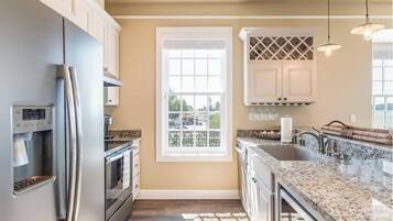 A modern kitchen with a stainless steel refrigerator, built-in oven, granite countertops, and a window with a view of the outdoors.