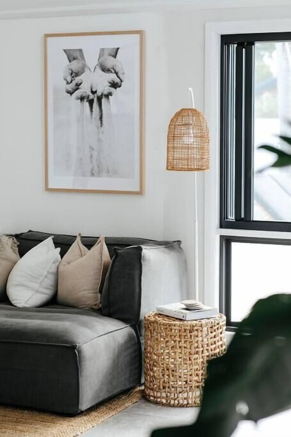 Una sala de estar moderna con un sofá gris, una obra de arte enmarcada, una mesita de noche tejida y una lámpara de pie.