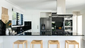 Een moderne keuken met een zwart aanrecht, roestvrijstalen apparatuur en drie houten krukken.