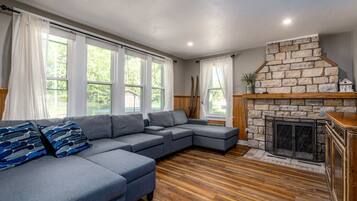 A modern living room with a stone fireplace, a sectional sofa, and large windows.