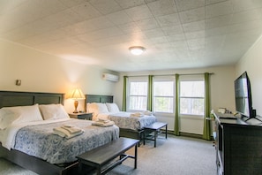 A hotel room with two beds, a desk, a TV, and a window with curtains.