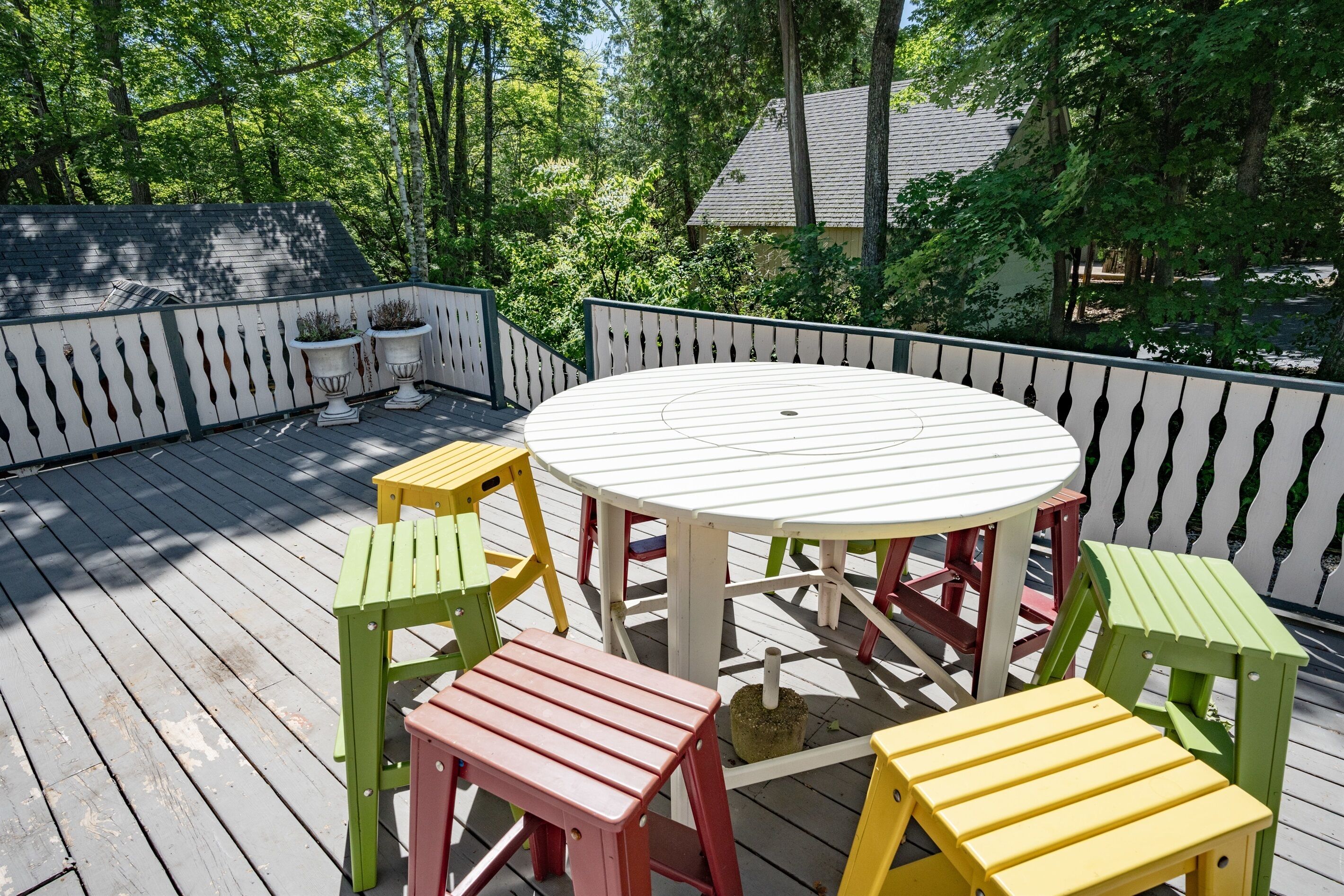 A wooden deck with a round table and colorful chairs, surrounded by a white picket fence.