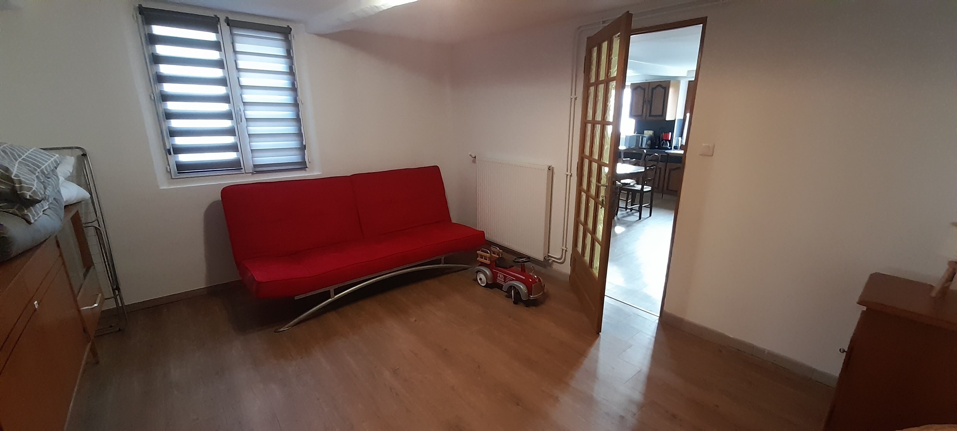 A room with a red sofa, a wooden cabinet, a radiator, and a toy car.