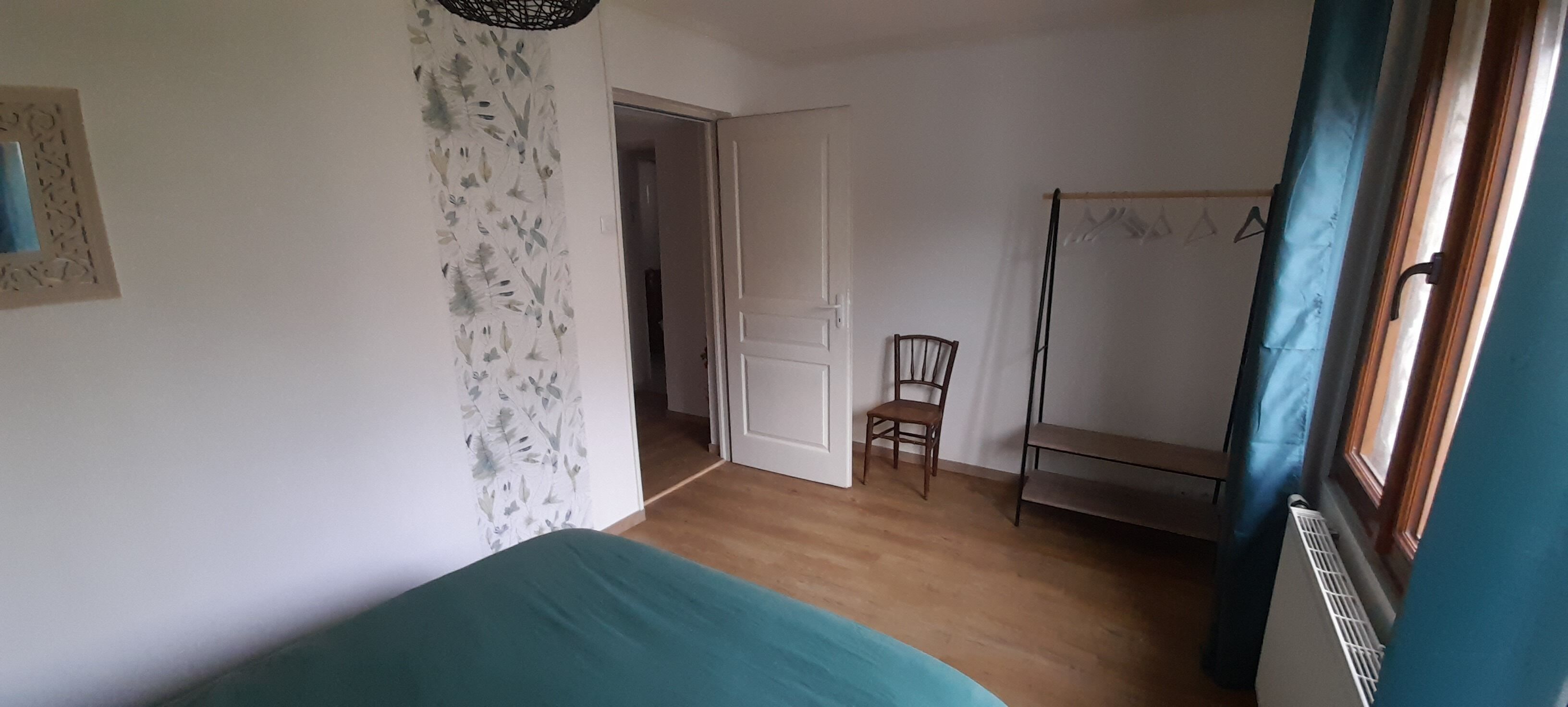 A room with a bed, a chair, a radiator, and a door leading to another room.