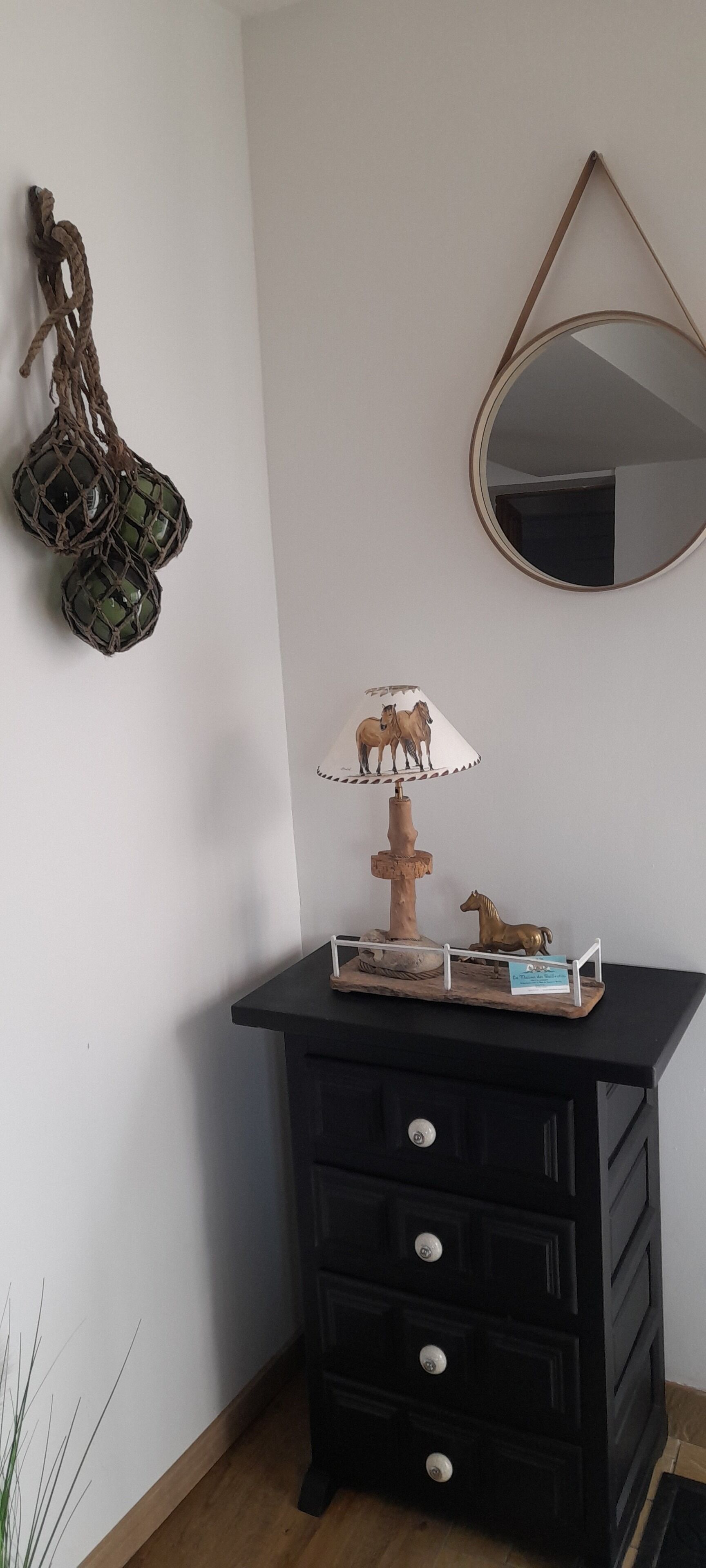 En hörna i ett rum med en svart byrå, en spegel, en lampa dekorerad med små hästfigurer och en repdekoration.