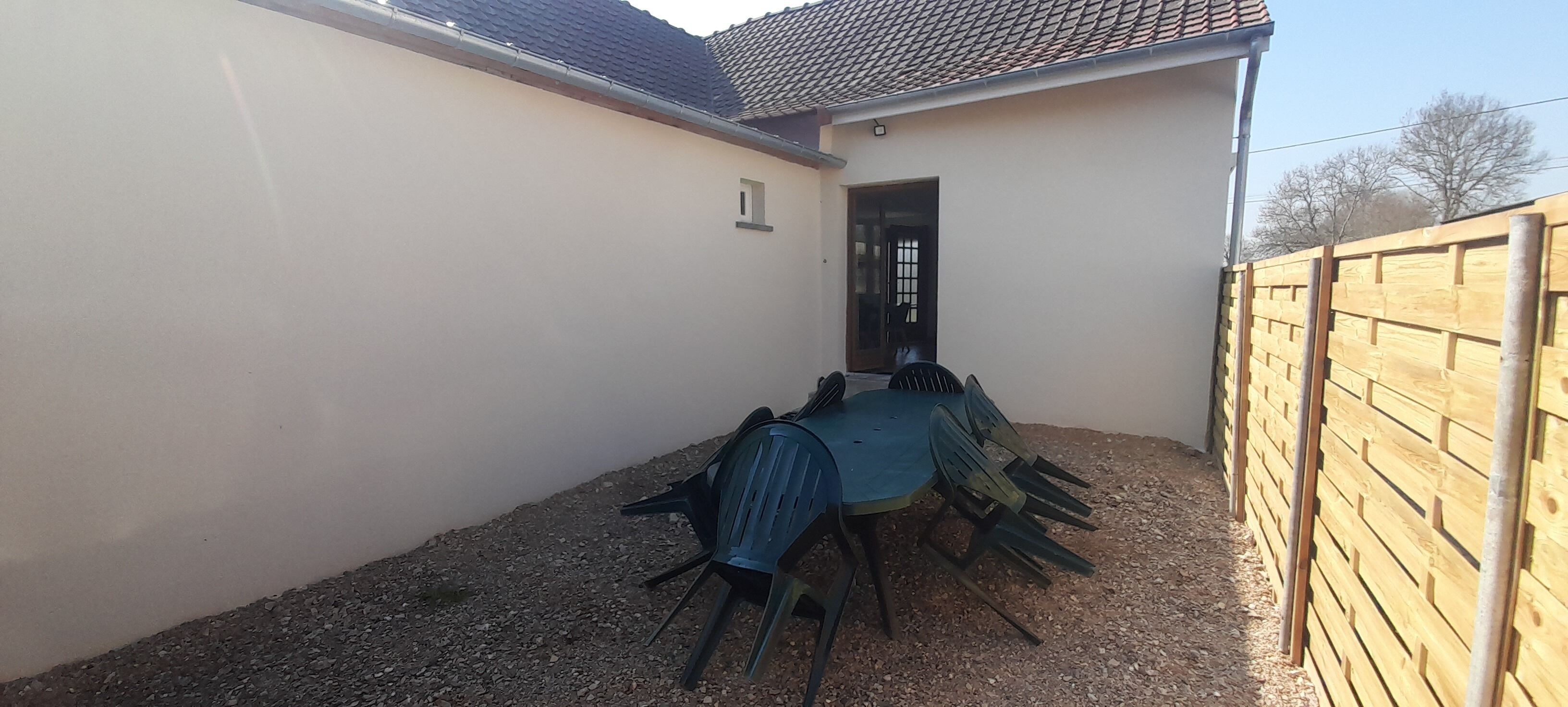A small outdoor patio with a table and chairs, a wooden fence, and a building with a tiled roof.