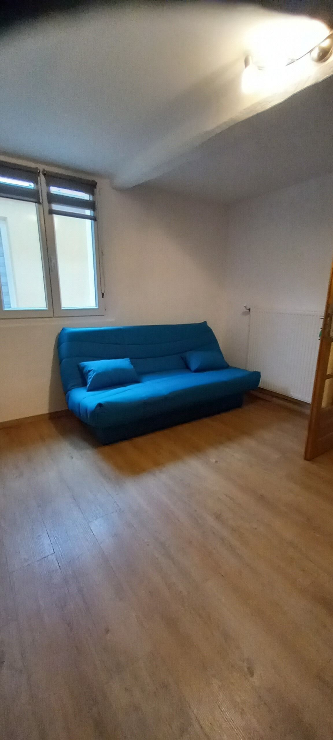 Ein Zimmer mit einem blauen Sofa, Holzboden, einem Fenster und einer Heizung.
