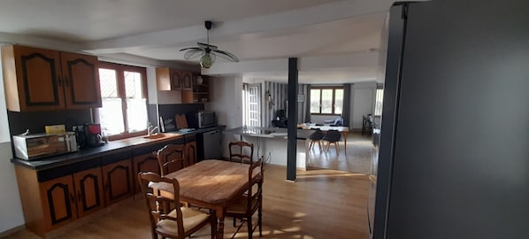 Une cuisine spacieuse avec des meubles de rangement en bois, une table à manger et des chaises. On y trouve également un four à micro-ondes et un ventilateur au plafond.