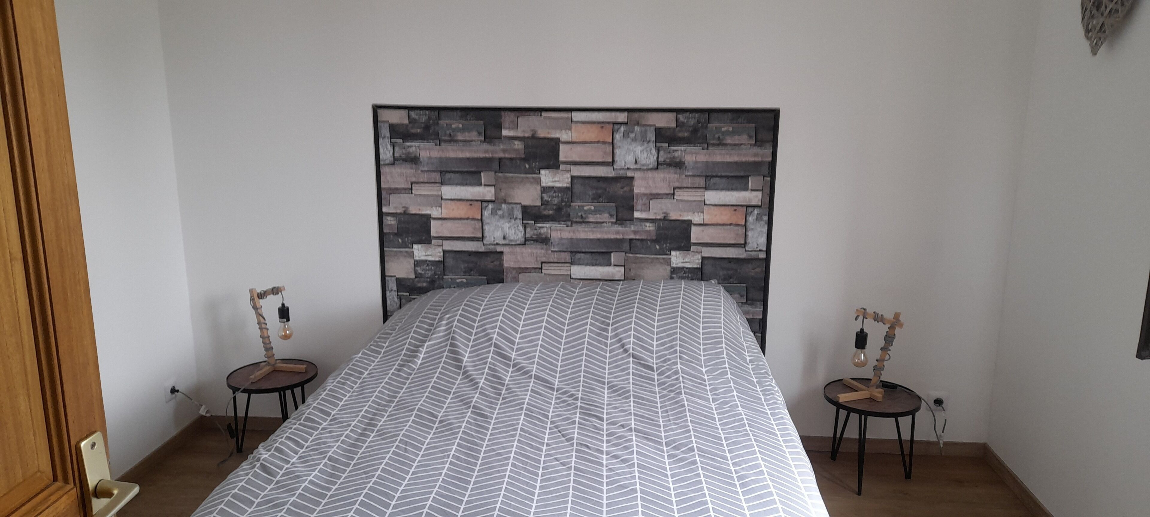A bedroom with a bed, a wall-mounted headboard, two bedside tables, and a small rug.