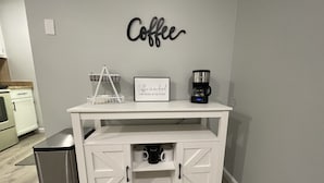 Una encimera de cocina blanca con una cafetera, un marco con una cita, y un cartel que dice 'Coffee'.