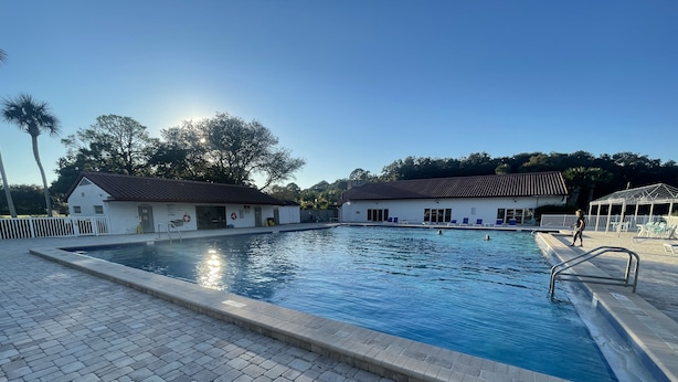Una piscina con solárium de azulejos, una torre de socorristas y una zona de estar cubierta.