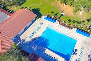Vue aérienne d’un hôtel doté d’une grande piscine, d’un bâtiment au toit rouge et d’un espace verdoyant agrémenté de palmiers.