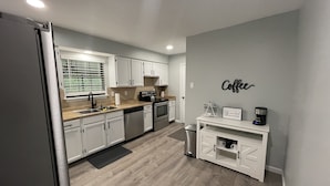 Una cocina moderna con armarios blancos, un refrigerador de acero inoxidable y una zona para café.