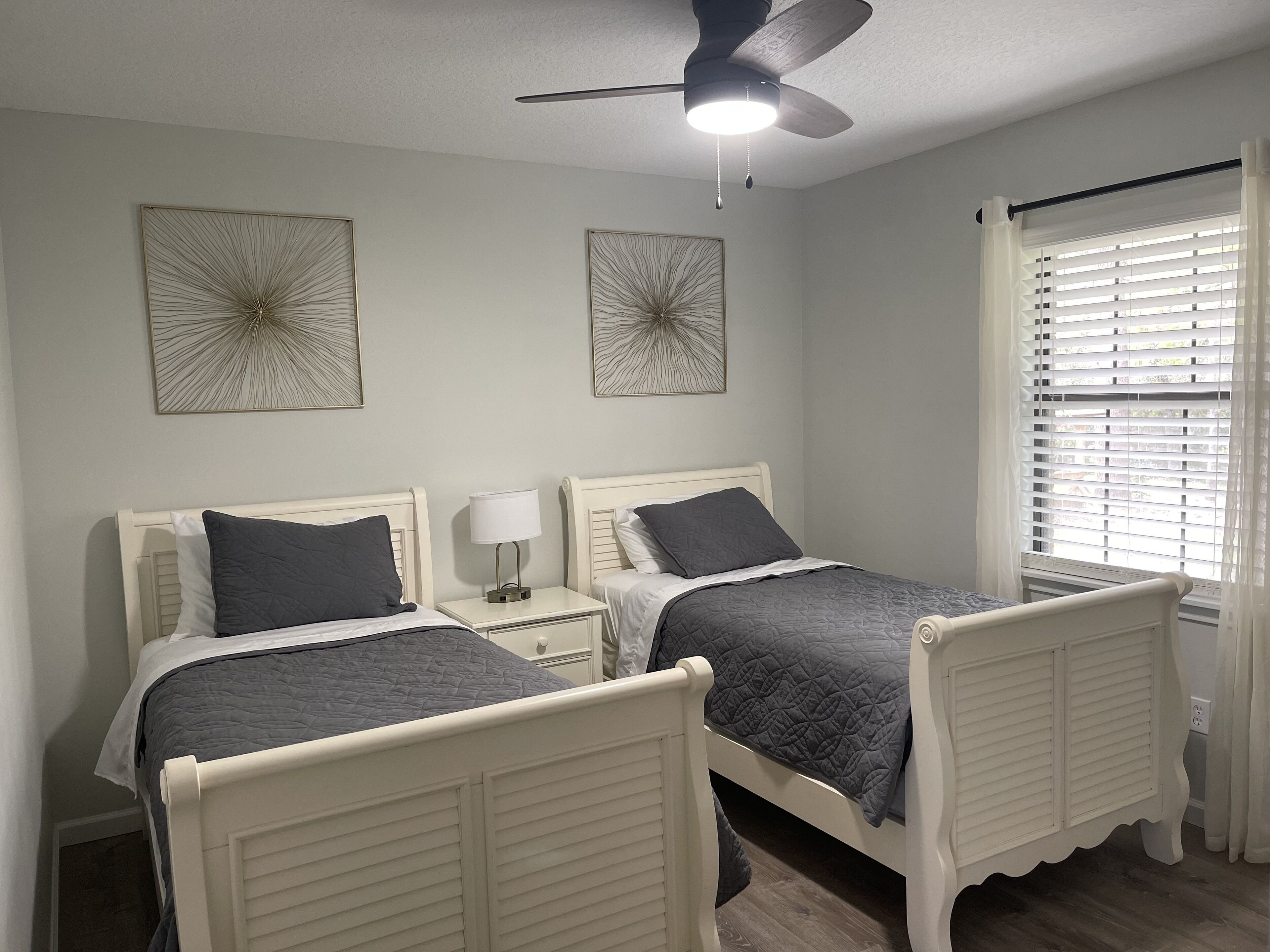 Ein Schlafzimmer mit zwei weißen Betten, einem Deckenventilator und Kunstwerken an den Wänden.