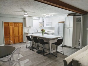 A modern kitchen with white cabinets, a central island with bar stools, a dining table with chairs, and a wooden door in the background. - Beautifully Renovated Space in Lawrenceville Home, WiFi, Smart TV in All Rooms! (Lawrenceville)