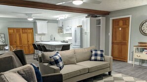 A living room with a sofa, armchairs, and a coffee table. There is a kitchen in the background with cabinets and appliances. - Beautifully Renovated Space in Lawrenceville Home, WiFi, Smart TV in All Rooms! (Lawrenceville)