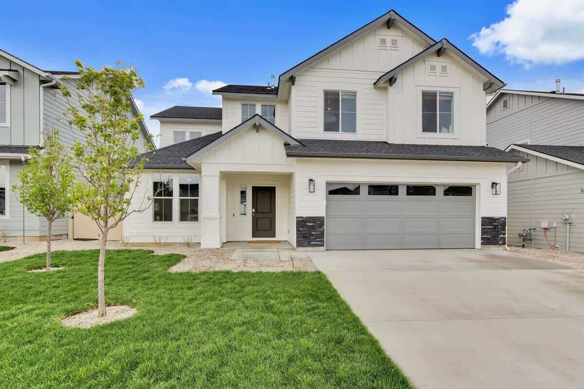 A two-story house with a garage, a small front yard with a tree, and a clear sky.