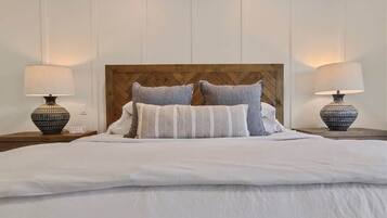 A neatly made bed with a wooden headboard, two bedside lamps, and a white wall with paneling.