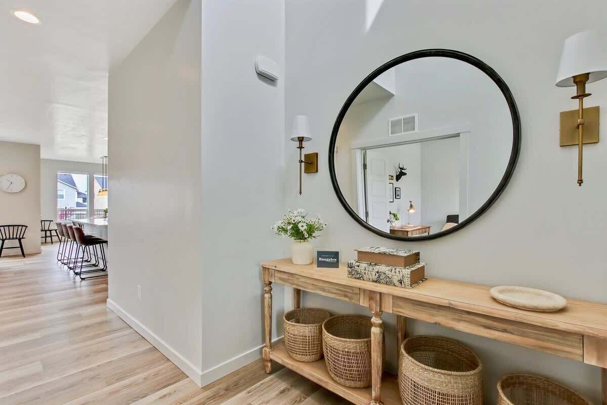 A modern interior with a wooden console table, wicker baskets, a round mirror, and a wall-mounted light fixture.