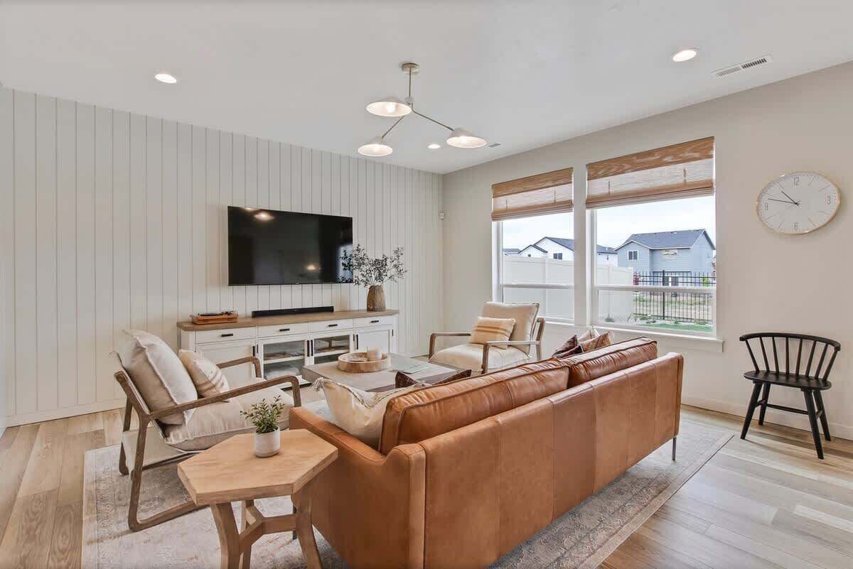A modern living room with a sofa, chairs, a coffee table, a TV, and a window with a view.