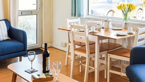 Uma área de refeições com uma mesa de madeira e cadeiras, uma garrafa de vinho e um copo na mesa.
