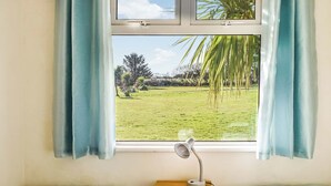 Quarto com duas camas, uma mesa de cabeceira, uma luminária de mesa e uma janela com cortinas.