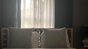 Una cama con dos almohadas, cabecera de madera y una ventana con cortinas estampadas.